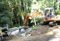 Excavator digging infiltration ditch. Truck at left is blowing rock into the trench.